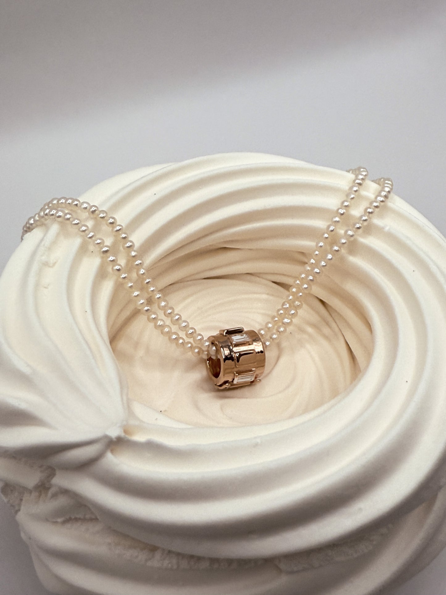 Elegant pendant necklace with a gold charm and pearl chain, set in a delicate swirl design background.