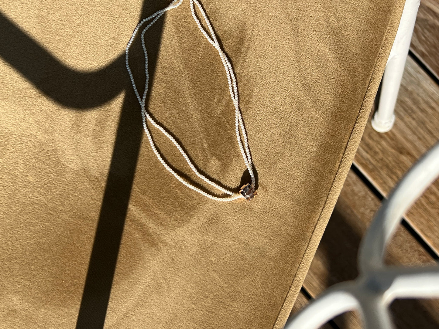 Elegant Emerald Éclair pendant surrounded by a delicate pearl necklace on a textured white surface.