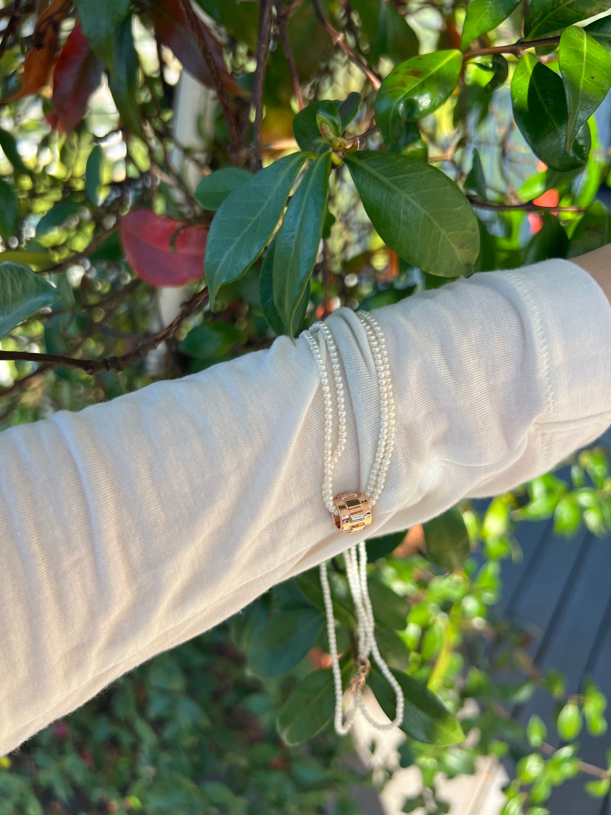 Elegant Emerald Éclair pendant surrounded by a delicate pearl necklace on a textured white surface.